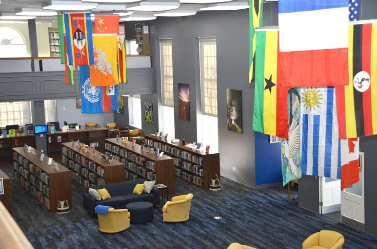 A bird's eye view of the library foyer. It includes comfortable chairs, rows of books, and international flags hanging from the ceiling