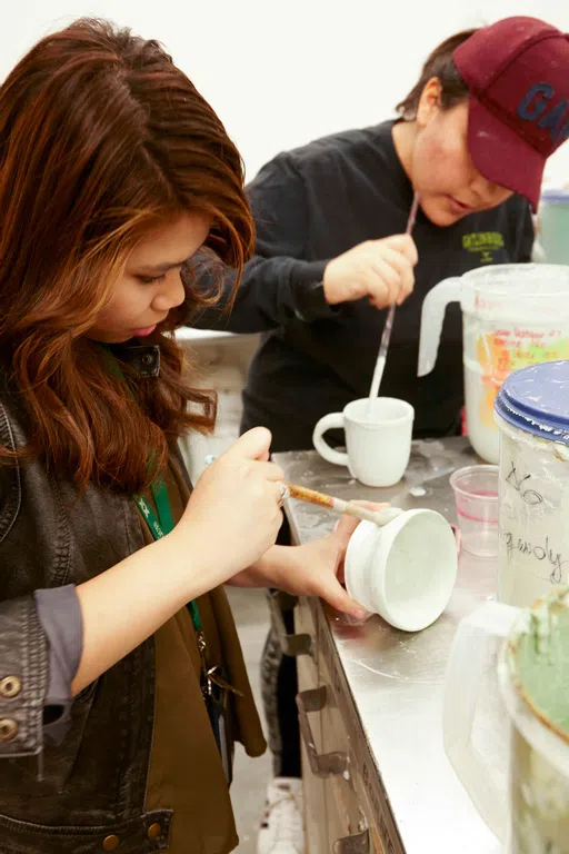 Two students painting hand-made mugs in pottery class