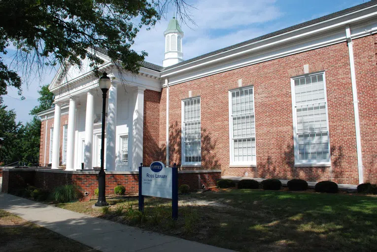 Tall windows, a series of roman columns, and white trim accentuate this long, brick building