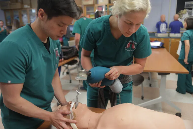 2 people in scrubs intibating a dummy