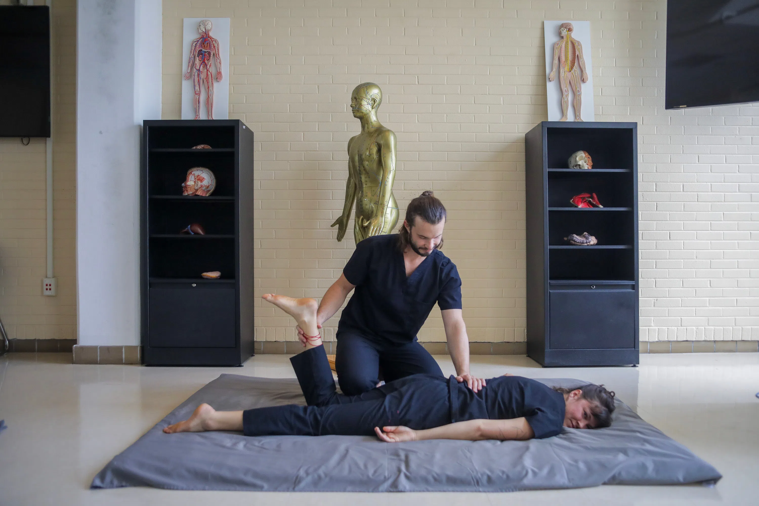 person on mat having leg stretched by another person, both in scrubs