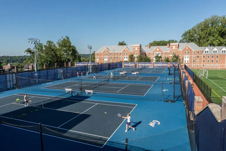 People playing tennis on courts in front of West Hall