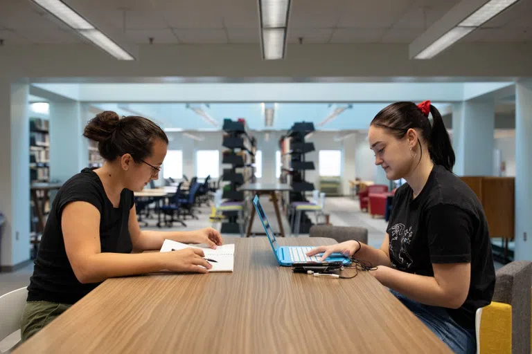 Students studying inside Eckles Library at a table with a notebook and laptop.  