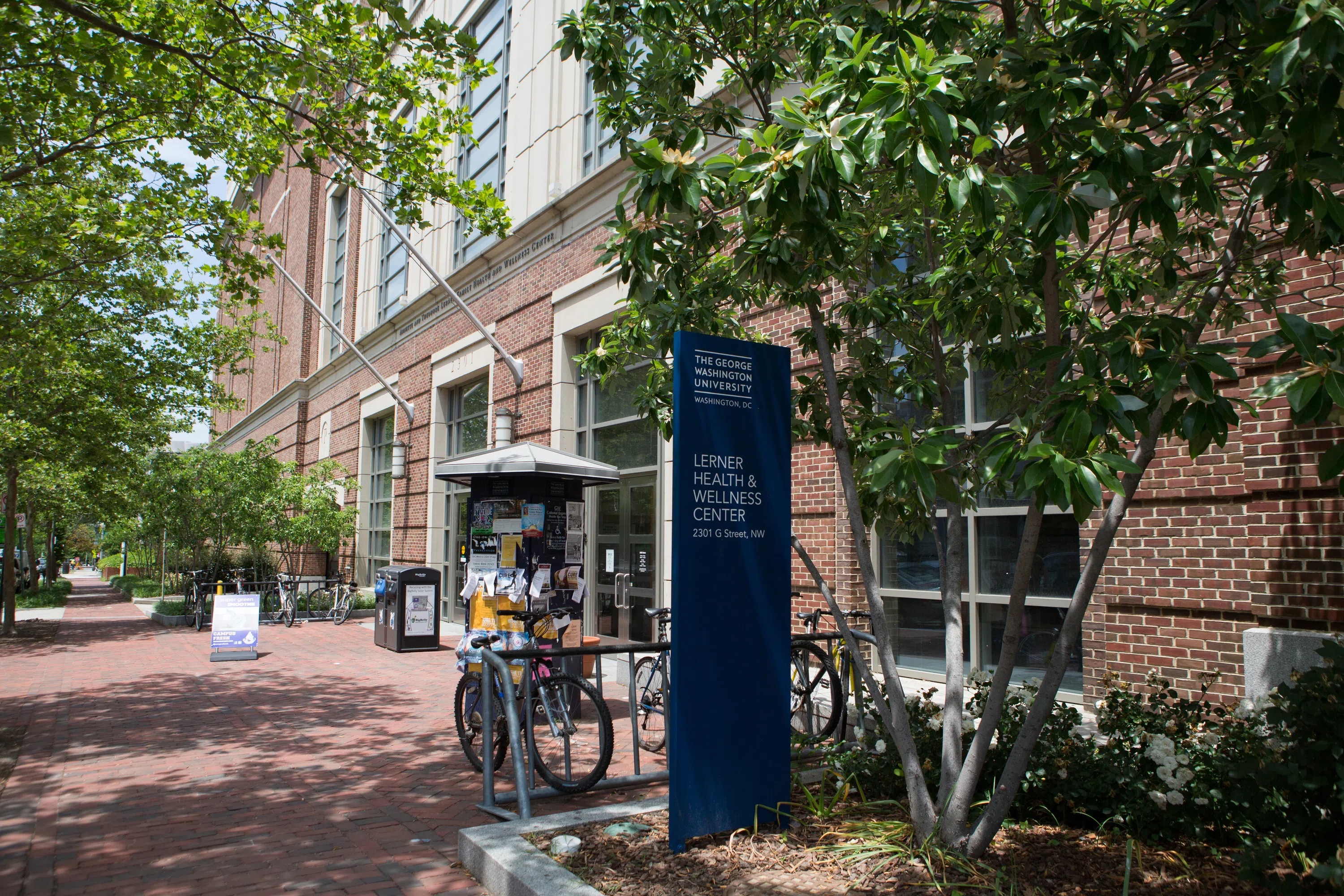 Exterior of Learner Health and Wellness Center with trees, bikes and a sign. 