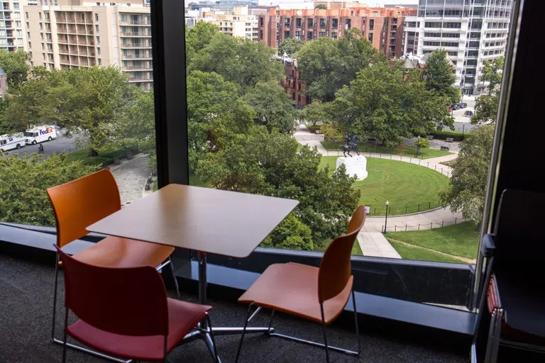 Green lawn and tree lined area outside a window with a table and chairs inside GW's School of Public Health