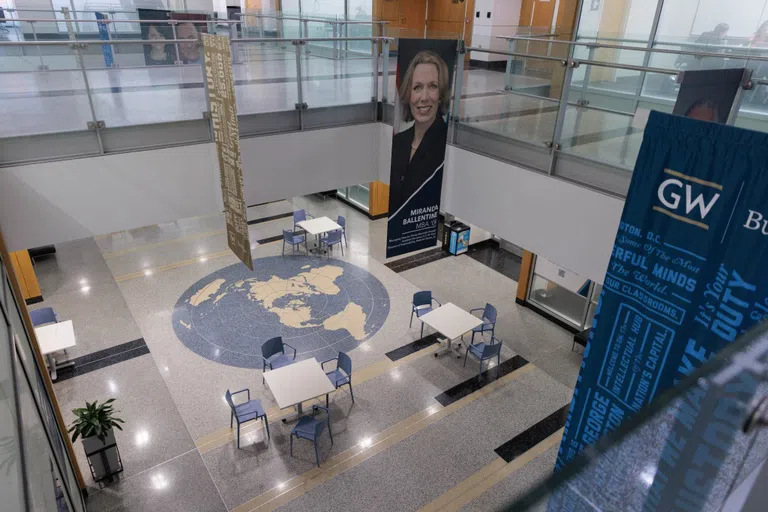 Glass paneled walkways overlooking tables and chairs on the floor below. 