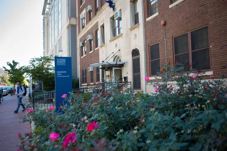 Student walking near a sign and flowers in front of Madison Hall 