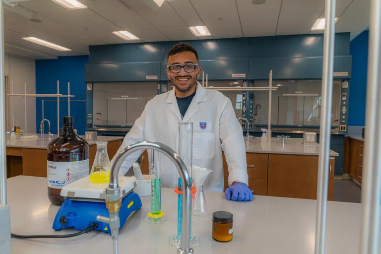 Student in lab coat smiles while conducting an experiment