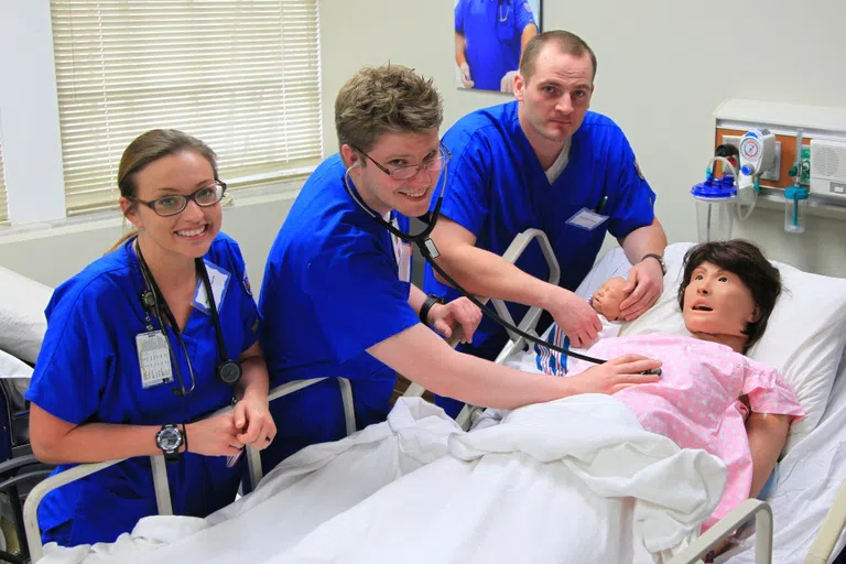 Students in the Nursing Simulation lab pose around a dummy patient in a hospital bed