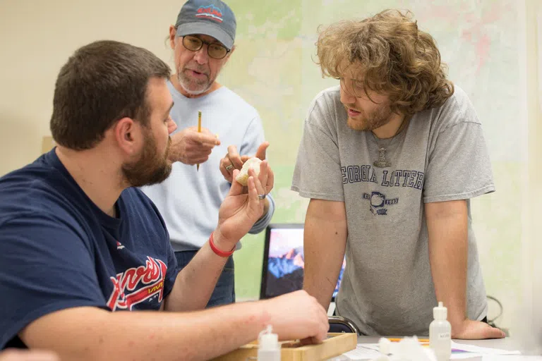 Two student examine a white rock with their professor 