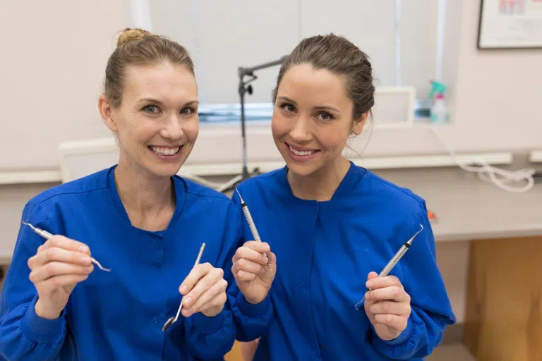 Two dental students smile and give thumbs up to the camera