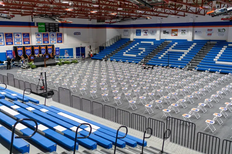 Gymnasium set up for graduation. Rows of chairs facing a stage with bleachers surrounding them