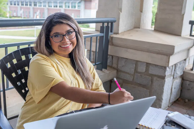 Student smiles for the camera while studying on the second floor patio