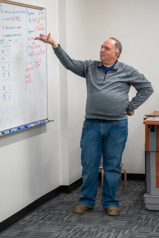 Professor stands at the whiteboard, pointing something out