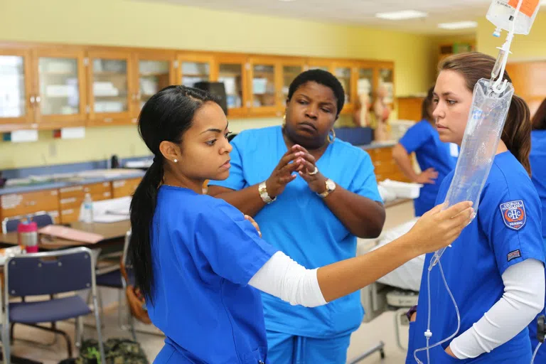 Nursing student checks fluids bag while other student and instructor look on