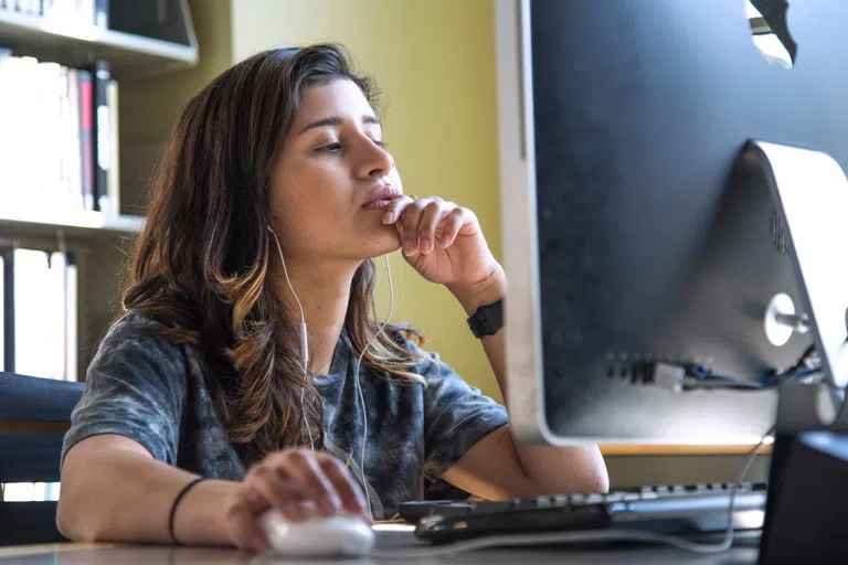 Student focuses on work in front of a desktop computer in the library