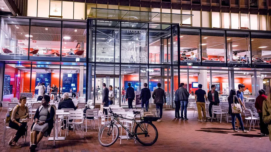 People sit at tables and stand outside of a glass building