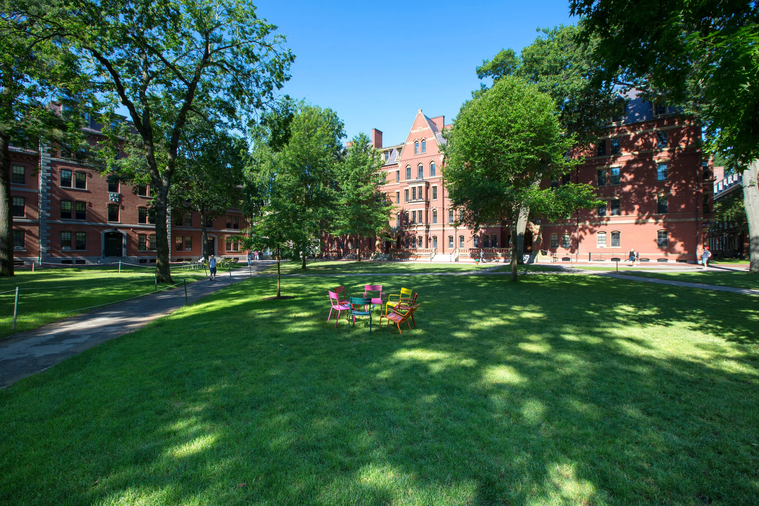 Colorful chairs sit in a circle on a grassy quad, with a red brick building in the distance