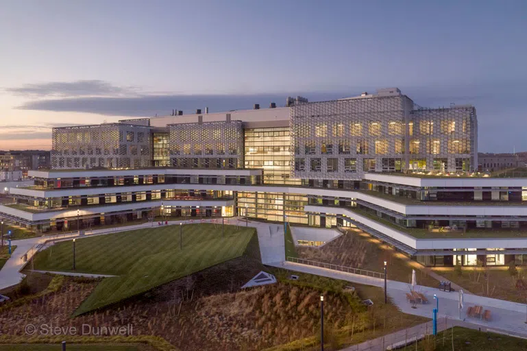 Aerial shot of silver windowed modern building. Grassy lawn in front.