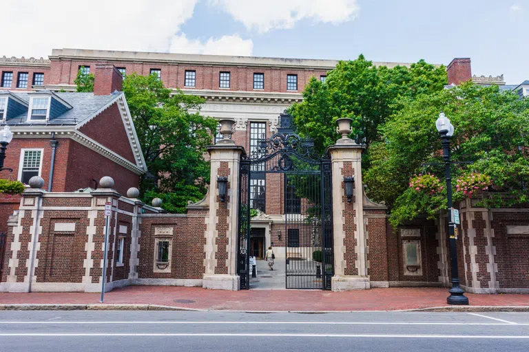 Red brick wall and iron gate gives entrance to Harvard Yard; large building inside gates