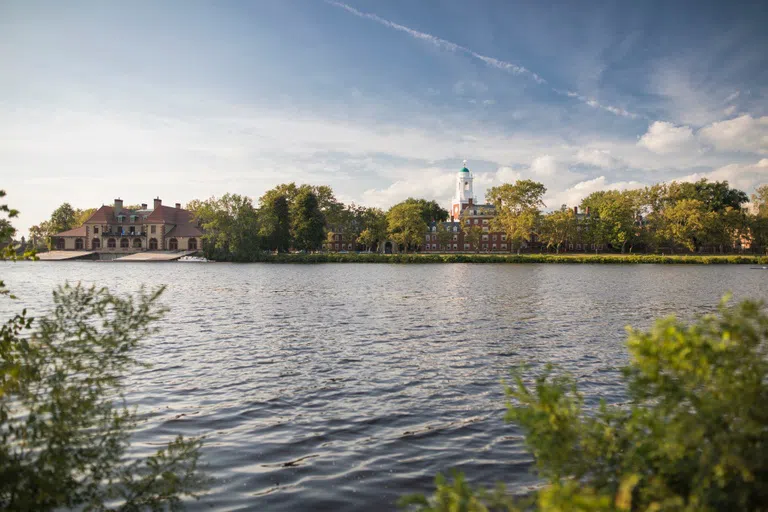 River water in the foreground with trees and dorms on the opposite river banks