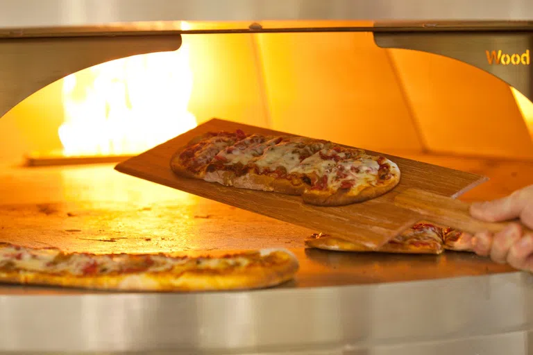 A pizza being placed inside a brick fire pizza oven