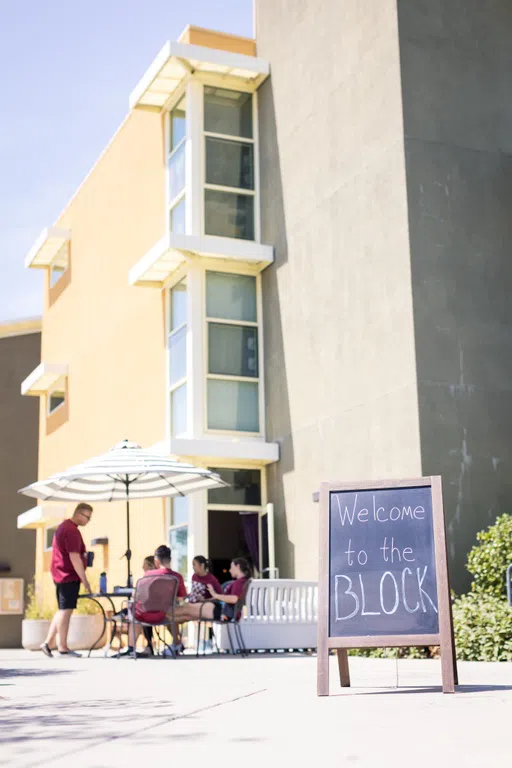 Students serated on a picnic table outside the black with a "welcome to the block" sign