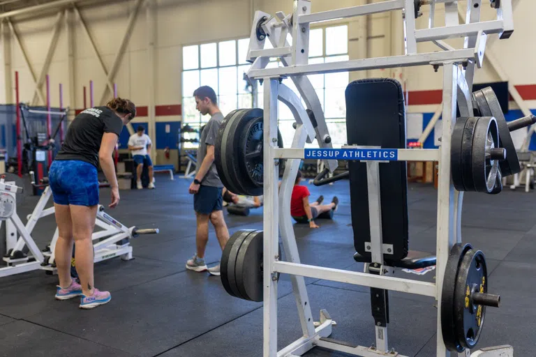 students exercising in the weight room next to weight-rack with "Jessup athletics" label