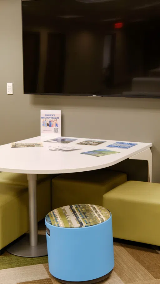 A white table with chairs and stools underneath a wall-mounted television.