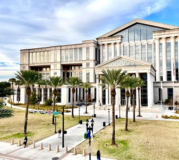 A large white building, with a paved, tree-lined walkway in front.