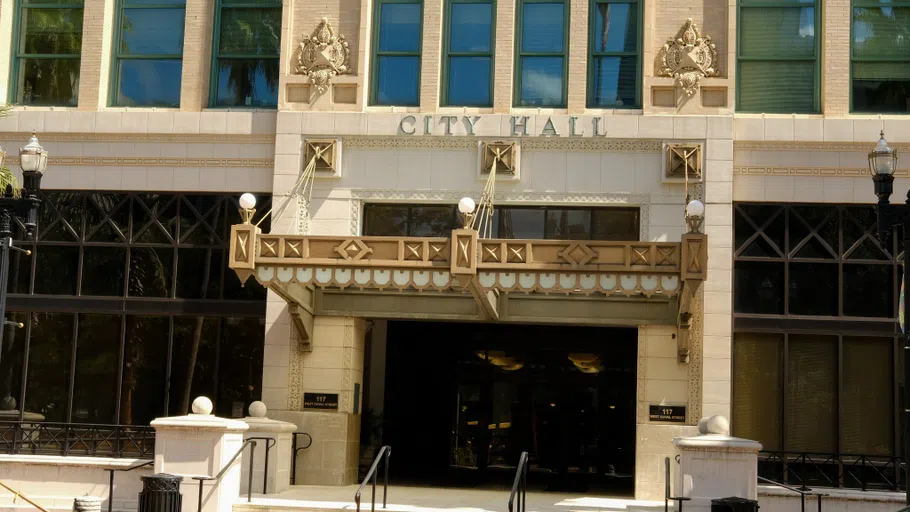 A beige building with gold trim and two large doors under a "city hall" sign.