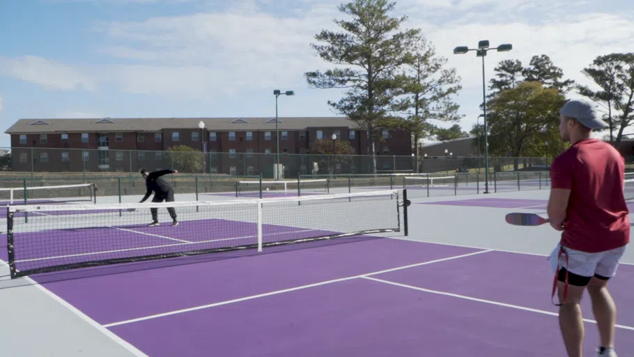 Students play tennis on a sunny day.