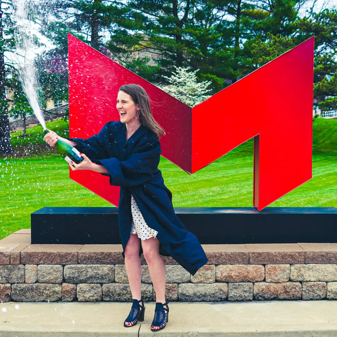 A recent Maryville graduate pops champagne in front of the Big Red "M"