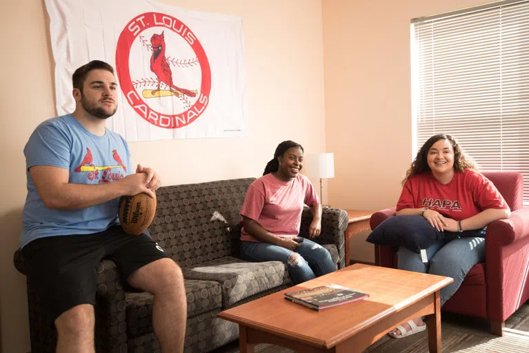 Students sit on the couch in an apartment watching TV. 