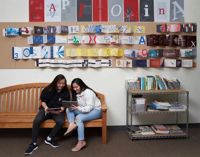 Graphic Design students work with student artwork in the background. 