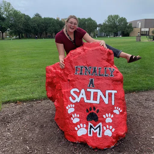 A student grab s a photo with the painted rock ("Finally a SAINT") to celebrate becoming a SAINT.