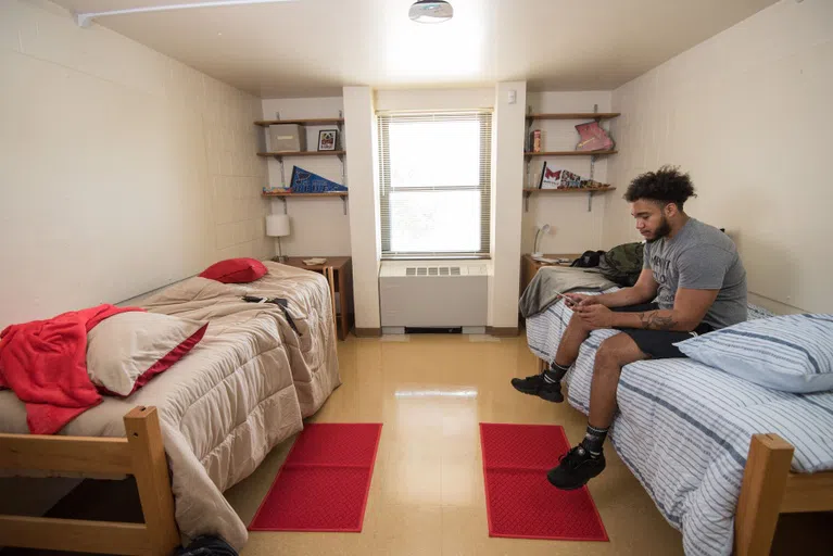 A student sits on a bed in one of the double rooms in Mouton Hall. 