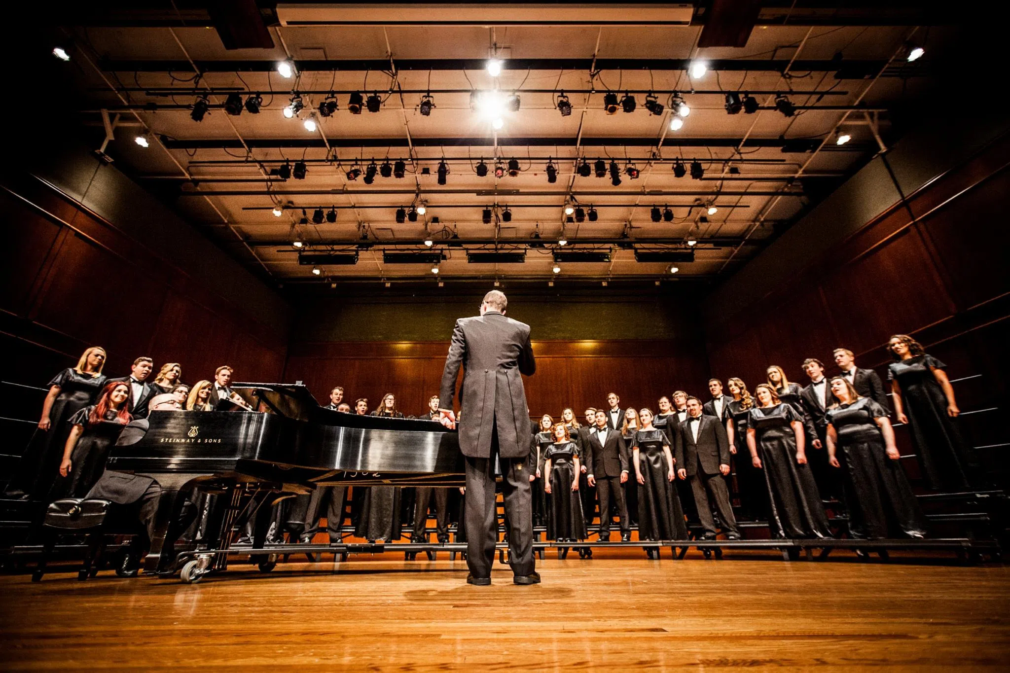 Conductor stands in front of a choir while they sing. The conductor's back is to the audience