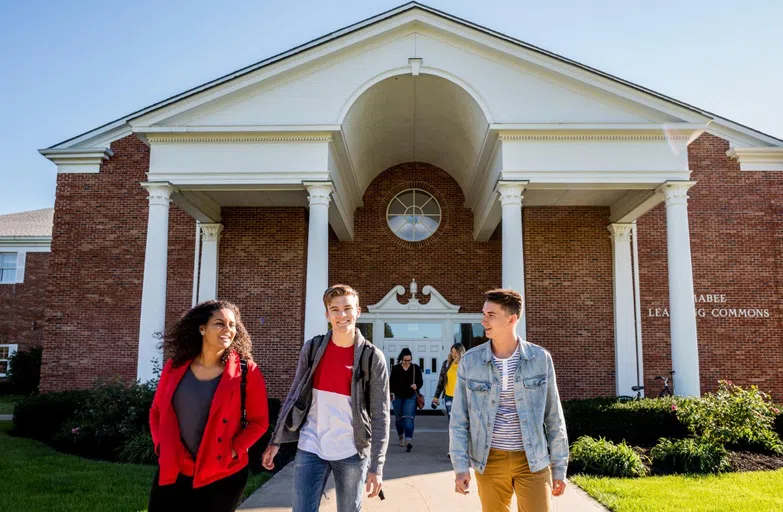 Three students walk out of the Mabee Commons' exterior entrance