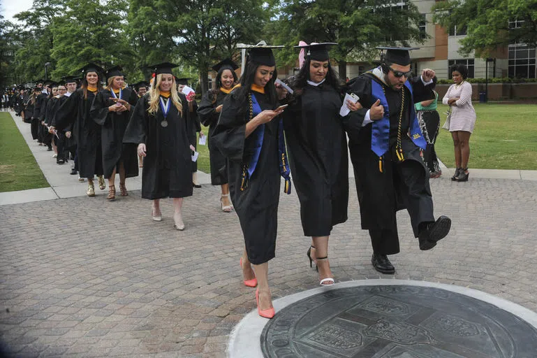 Students walk on the seal during commencement