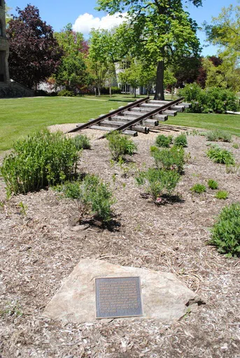 A photo of the sculpture of the Underground Railroad, a rail angled up into the air which is buried.