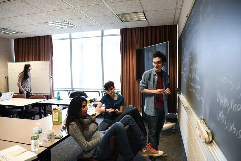 A group of 3 students use the chalk board in King Building to quiz each other on Latin translations.