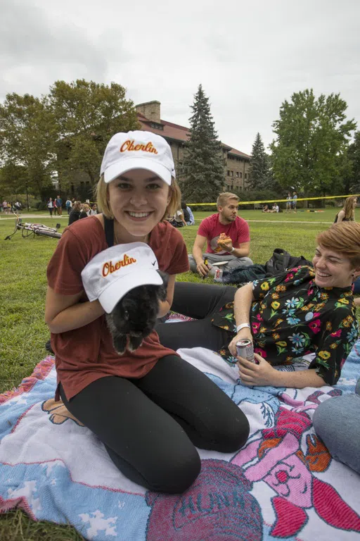 A smiling student shows her rabbit, wearing an Oberlin baseball cap.