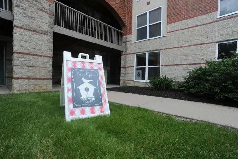 A sandwich board sign placed on a sidewalk indicates the location of the Promise House.