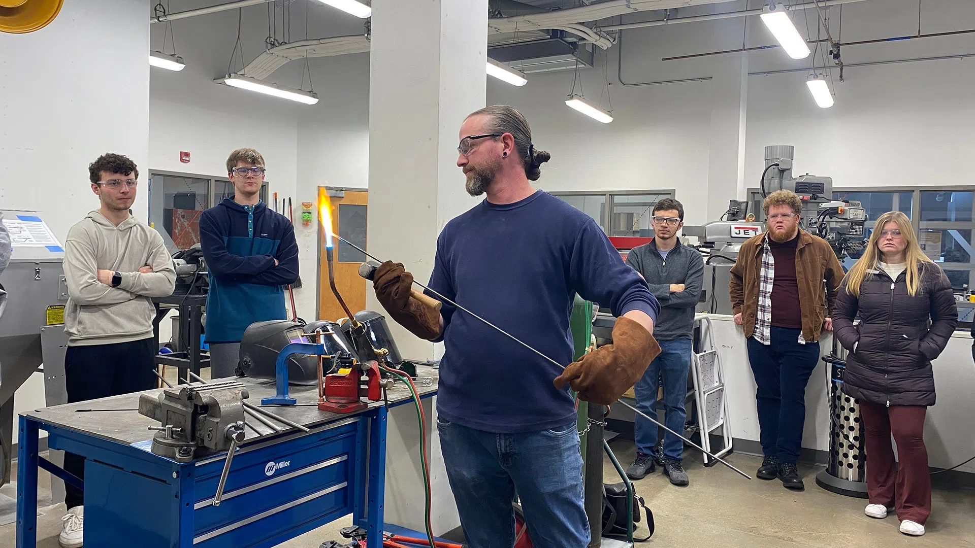 A man heats an iron rod over a blowtorch