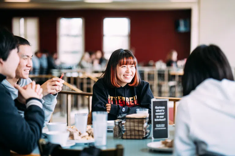 A happy group of students sit together in the Campus Center dining area.