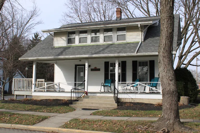 White building with grey roof. There is a porch with chairs out front.