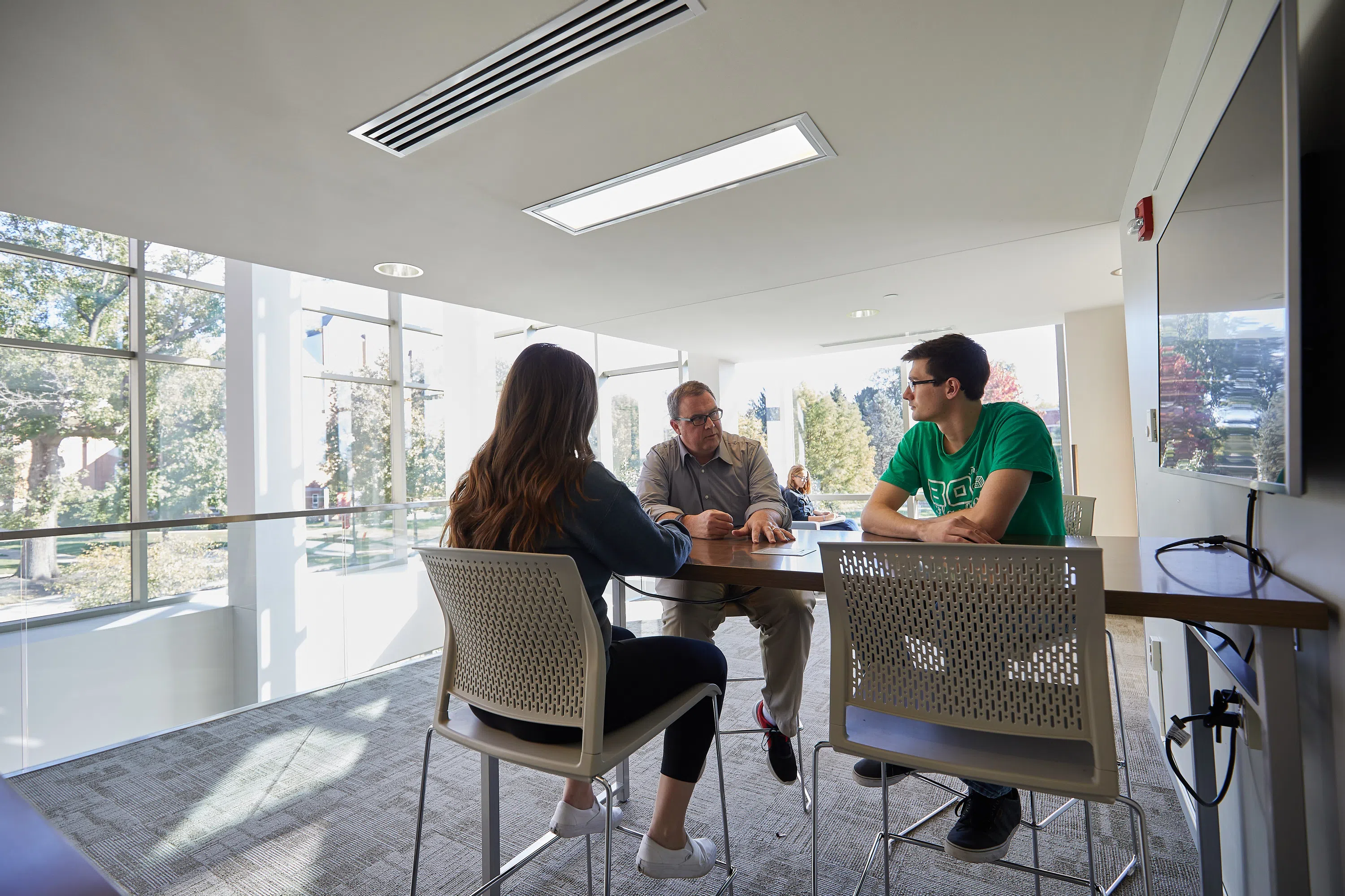 A faculty member sits at a table with two students at the Shear-McFadden Science Center.