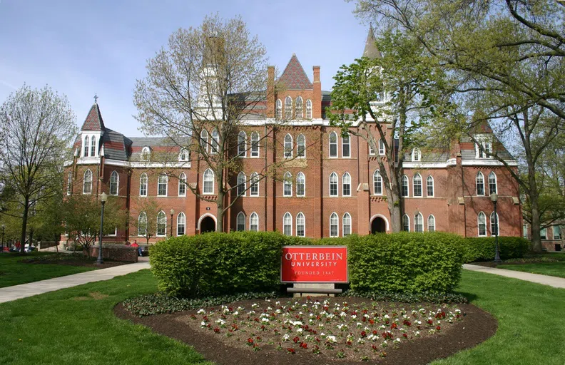 Front view of Tower Hall and grounds. A four story brick buidling with two bell towers near the central area of the facade.