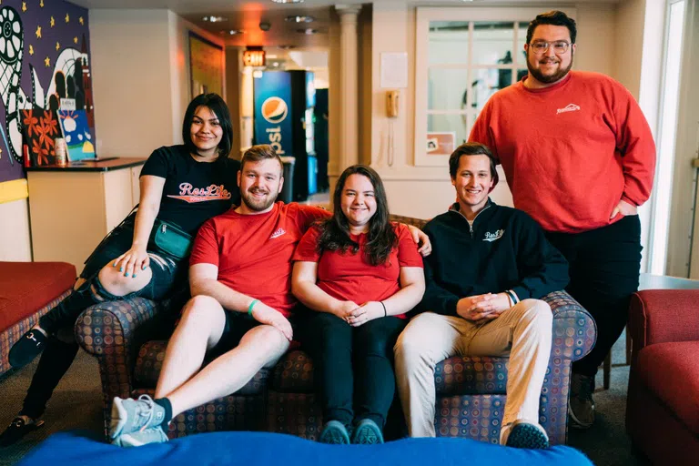 RAs sit together for a group photo in a cozy residence hall lounge.